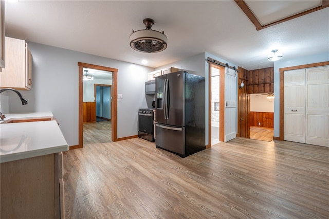 kitchen featuring sink, stainless steel refrigerator with ice dispenser, a barn door, light hardwood / wood-style flooring, and black range oven