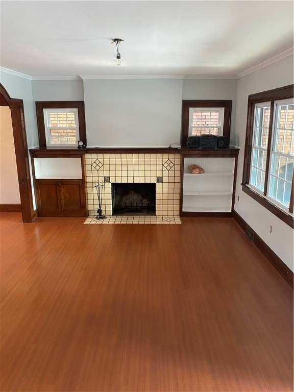 unfurnished living room featuring a tile fireplace, ornamental molding, and hardwood / wood-style flooring