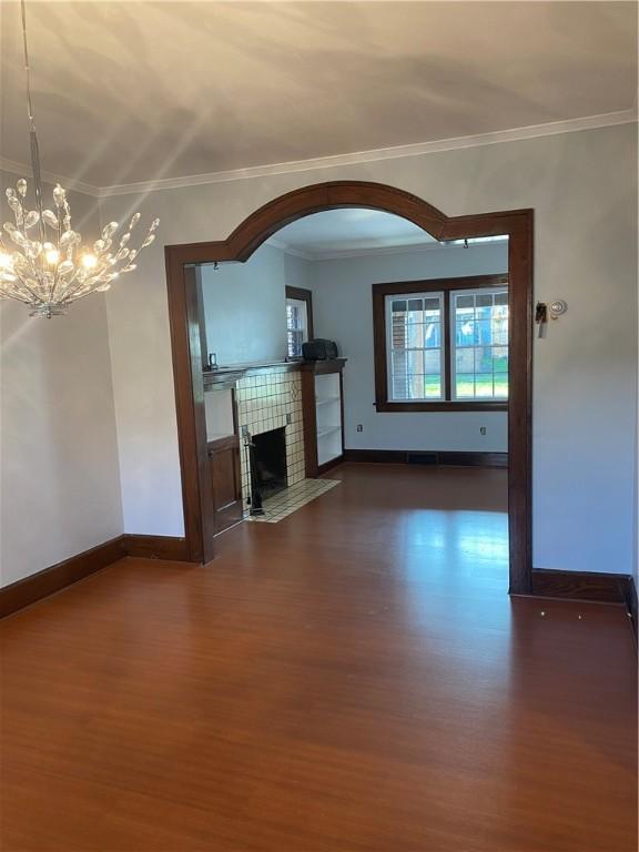 unfurnished living room with an inviting chandelier, a tile fireplace, dark hardwood / wood-style floors, and crown molding