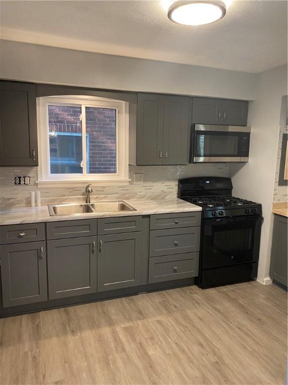 kitchen with black gas stove, sink, gray cabinets, light wood-type flooring, and decorative backsplash