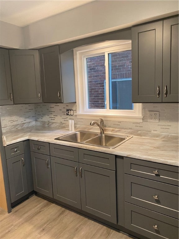 kitchen with light hardwood / wood-style flooring, decorative backsplash, gray cabinetry, and sink