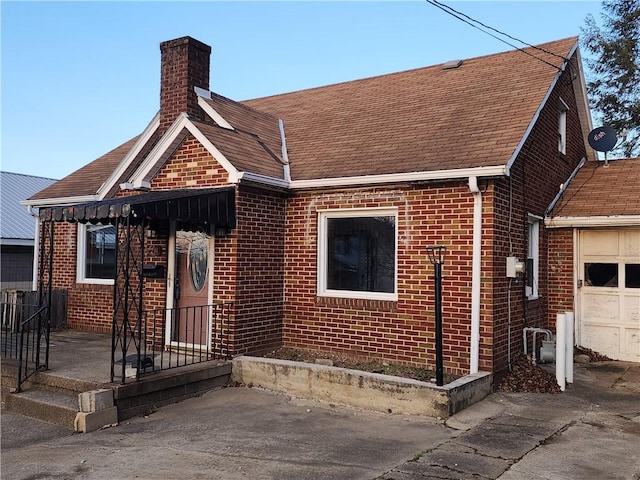 view of front of home featuring a shingled roof, brick siding, a chimney, and a garage