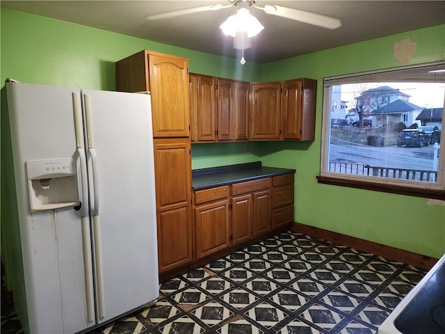 kitchen featuring dark floors, baseboards, brown cabinets, white fridge with ice dispenser, and dark countertops