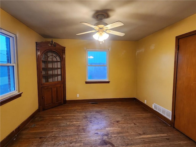 unfurnished room with a ceiling fan, visible vents, baseboards, and wood finished floors