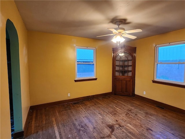 spare room featuring ceiling fan, arched walkways, wood finished floors, visible vents, and baseboards