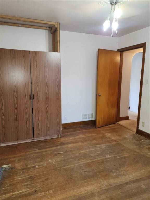 interior space featuring wood-type flooring, visible vents, arched walkways, and baseboards