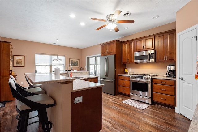 kitchen with sink, decorative light fixtures, appliances with stainless steel finishes, a kitchen bar, and dark hardwood / wood-style flooring