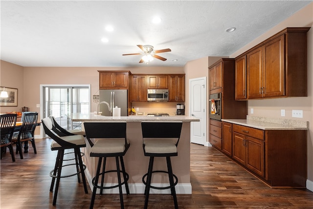 kitchen featuring an island with sink, appliances with stainless steel finishes, dark hardwood / wood-style flooring, and ceiling fan