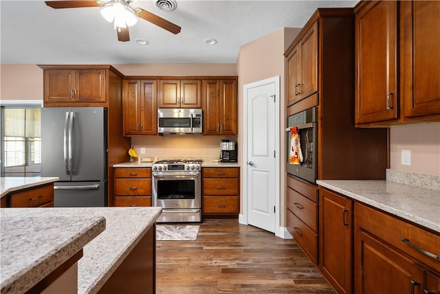 kitchen with light stone countertops, dark hardwood / wood-style floors, appliances with stainless steel finishes, and ceiling fan