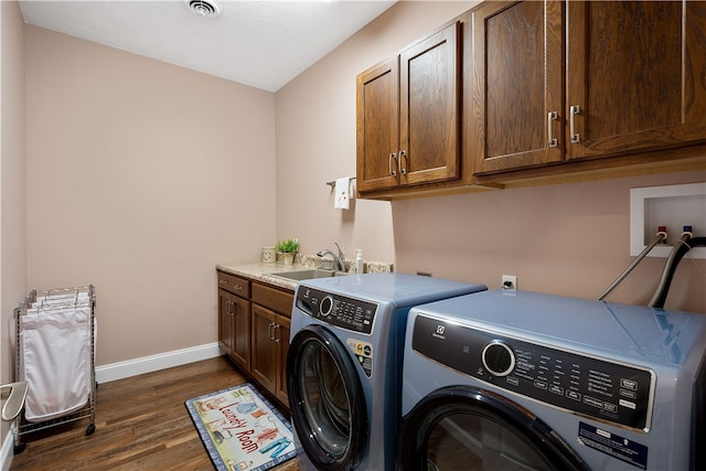 clothes washing area with washer and clothes dryer, cabinets, dark wood-type flooring, and sink