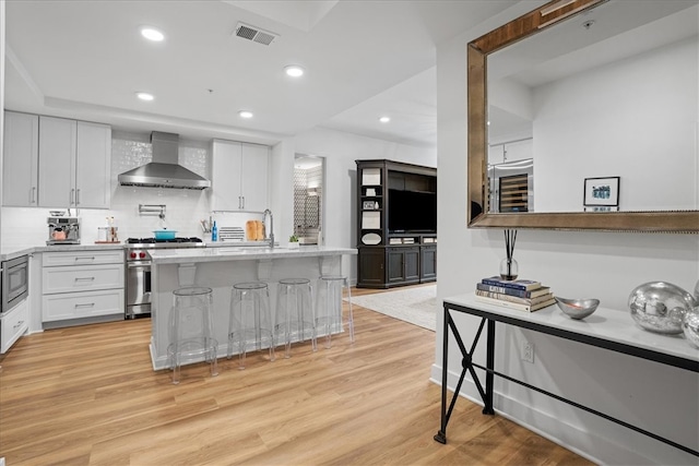 kitchen with wall chimney exhaust hood, stainless steel appliances, a kitchen breakfast bar, and white cabinets