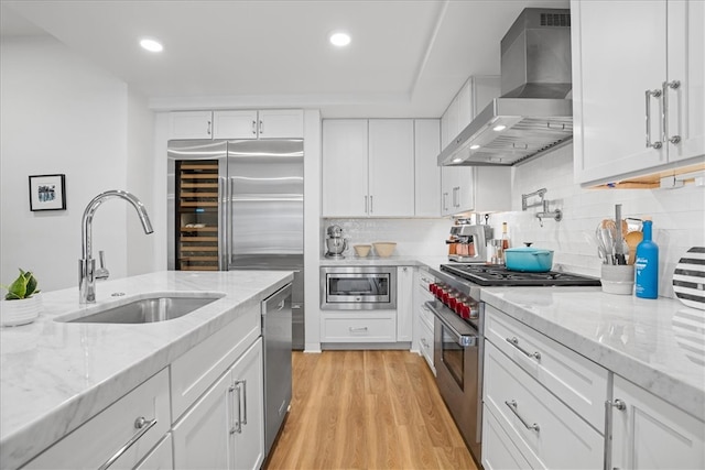 kitchen featuring white cabinetry, built in appliances, light hardwood / wood-style flooring, sink, and wall chimney range hood