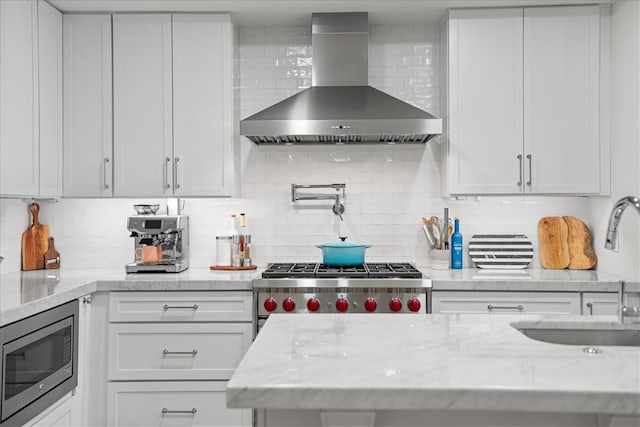 kitchen featuring appliances with stainless steel finishes, wall chimney range hood, and white cabinets