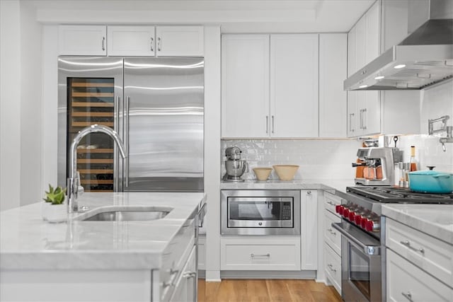 kitchen featuring light hardwood / wood-style floors, built in appliances, white cabinetry, wall chimney range hood, and decorative backsplash