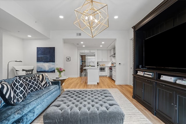 living room with a notable chandelier, light hardwood / wood-style flooring, and sink