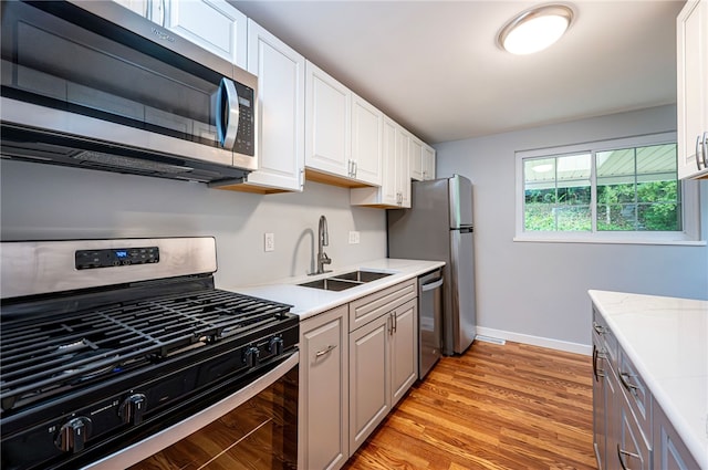 kitchen with light hardwood / wood-style floors, stainless steel appliances, sink, and white cabinetry