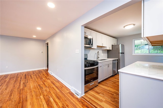 kitchen with sink, appliances with stainless steel finishes, white cabinetry, and light hardwood / wood-style flooring