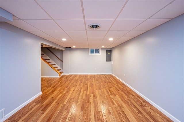 basement with a drop ceiling, hardwood / wood-style floors, and electric panel