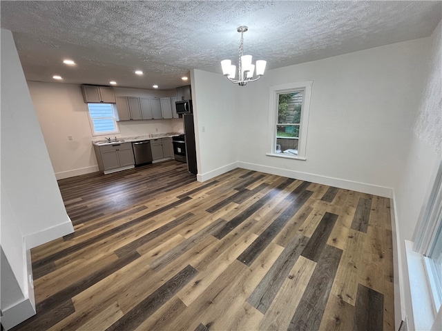 unfurnished living room featuring a notable chandelier, dark wood-type flooring, a textured ceiling, and a healthy amount of sunlight