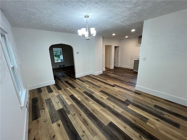 spare room featuring a textured ceiling, dark wood-type flooring, and a chandelier