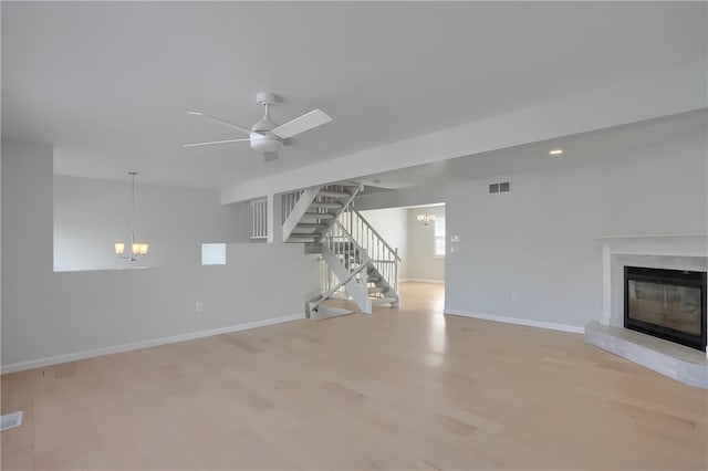 unfurnished living room featuring ceiling fan with notable chandelier, a high end fireplace, and light hardwood / wood-style floors