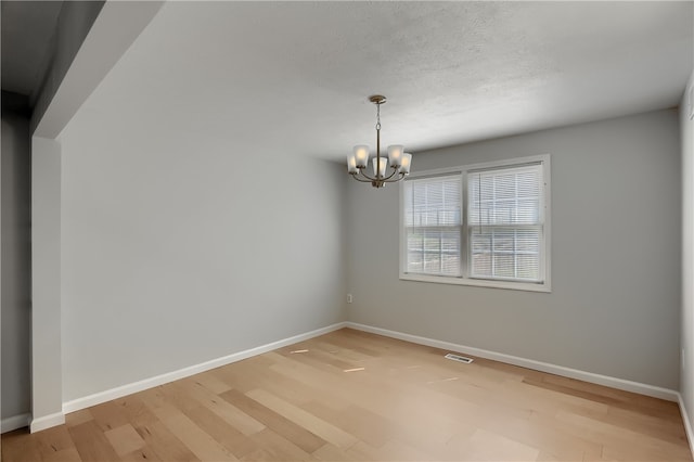 empty room with a notable chandelier and light hardwood / wood-style floors