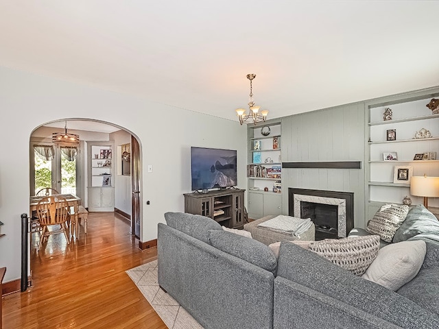 living room featuring light wood-type flooring, a chandelier, built in shelves, and a fireplace