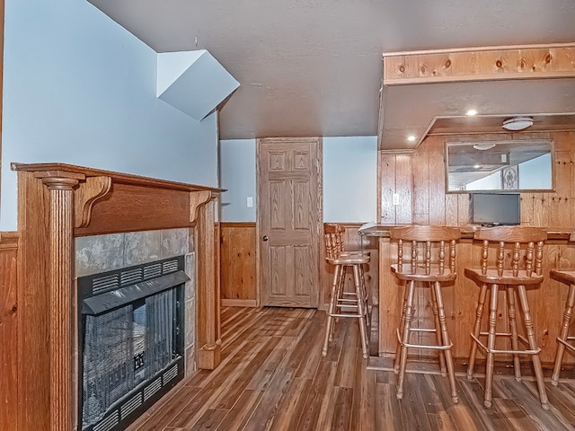 kitchen with hardwood / wood-style flooring, a tiled fireplace, and wood walls