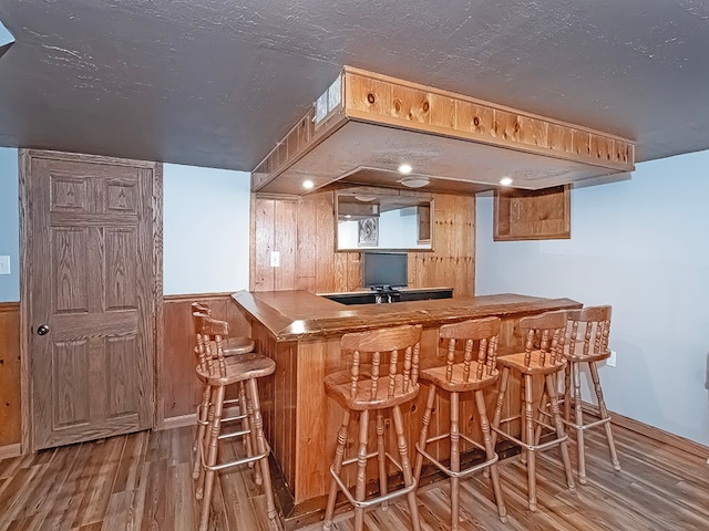 bar with a textured ceiling, wooden walls, and hardwood / wood-style flooring