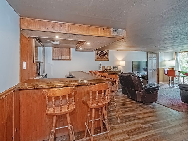 bar featuring hardwood / wood-style flooring, wood walls, and a textured ceiling