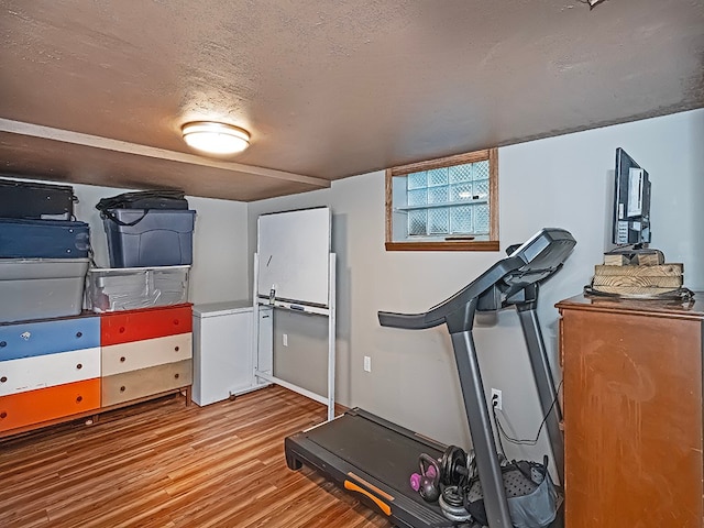 exercise room featuring light wood-type flooring and a textured ceiling