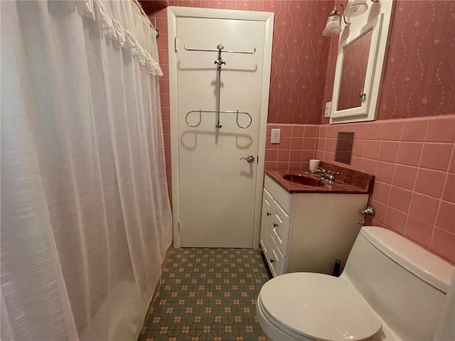 full bathroom featuring wallpapered walls, toilet, a wainscoted wall, tile walls, and vanity