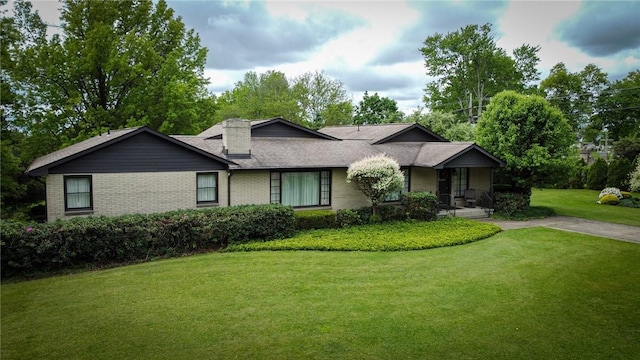 view of front of home featuring a front yard, brick siding, a chimney, covered porch, and a shingled roof