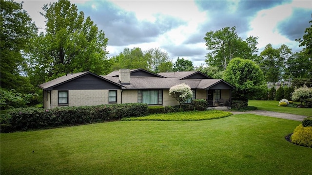 view of front facade with a front yard, a chimney, and brick siding