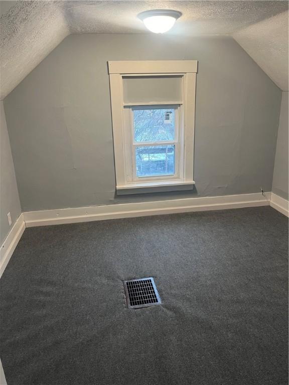 bonus room featuring a textured ceiling, lofted ceiling, and dark carpet