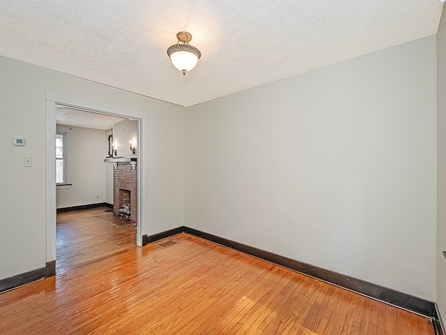 empty room featuring a brick fireplace, a textured ceiling, and hardwood / wood-style floors