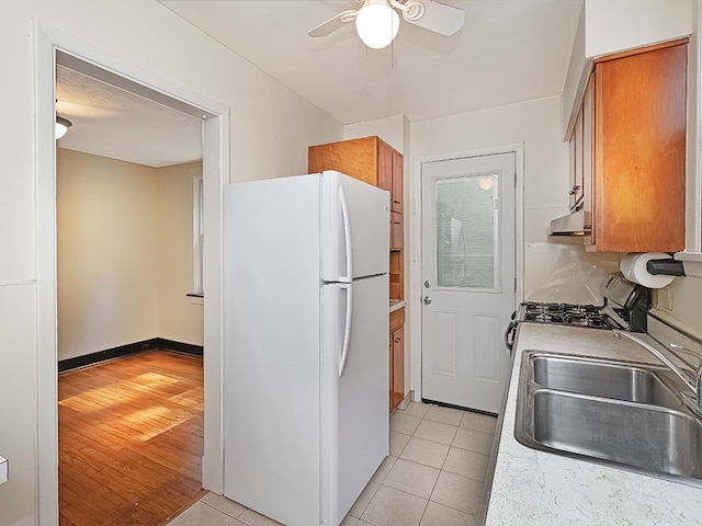 kitchen featuring white refrigerator, sink, stainless steel range with gas stovetop, light hardwood / wood-style flooring, and ceiling fan