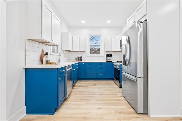 kitchen with appliances with stainless steel finishes, decorative backsplash, white cabinetry, light hardwood / wood-style flooring, and sink