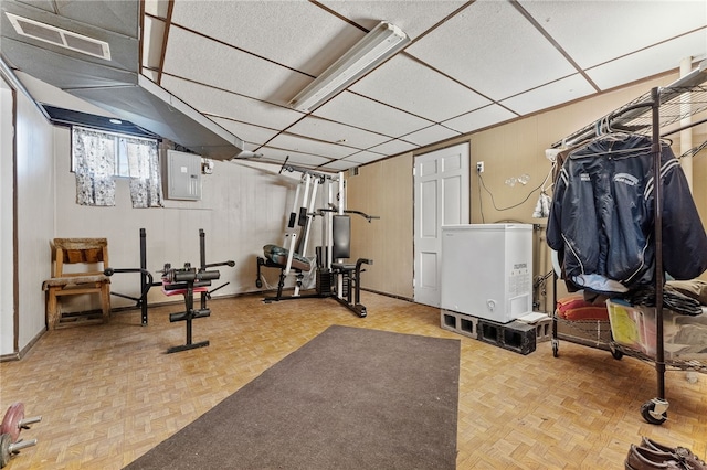 exercise area with wood walls, electric panel, and parquet flooring