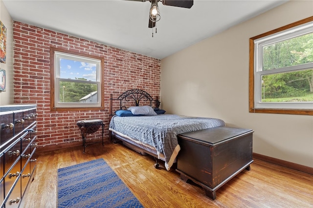 bedroom featuring ceiling fan, multiple windows, brick wall, and hardwood / wood-style floors