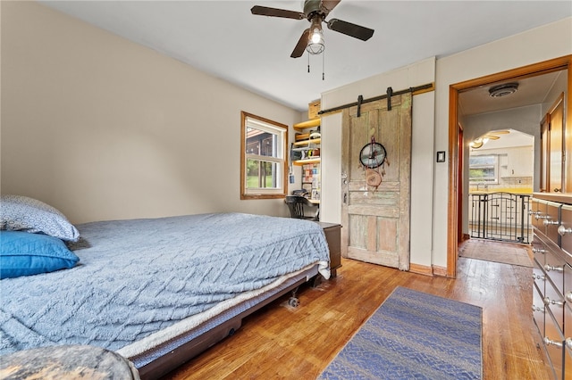 bedroom featuring ceiling fan, hardwood / wood-style flooring, a barn door, and multiple windows