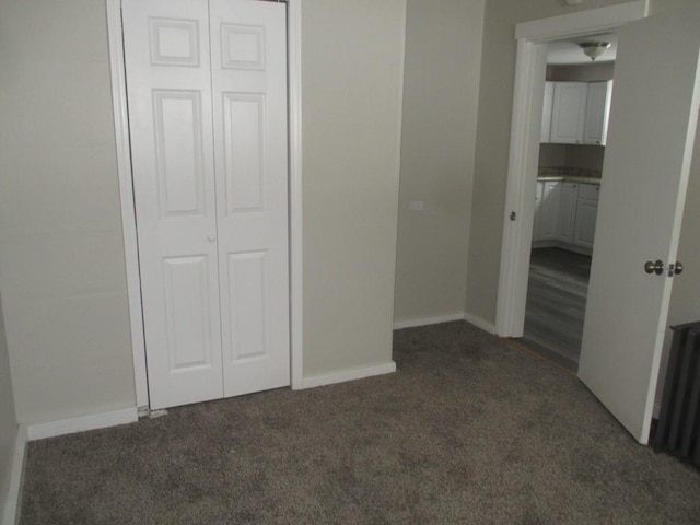 unfurnished bedroom featuring dark colored carpet, radiator heating unit, and a closet