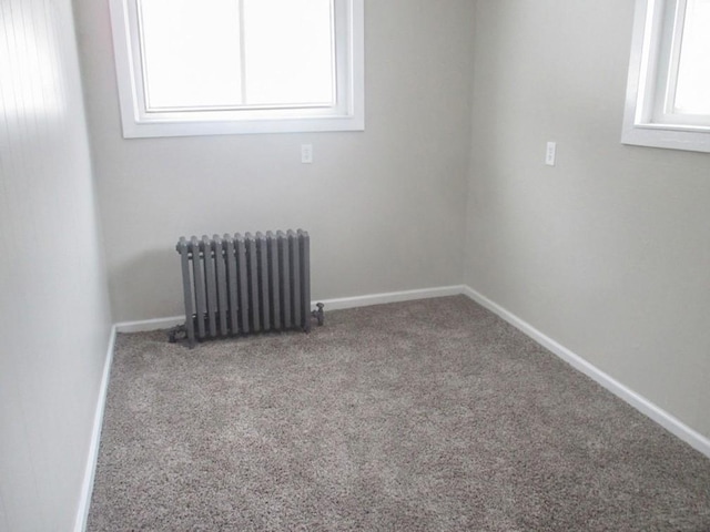 carpeted empty room featuring radiator heating unit, baseboards, and a wealth of natural light