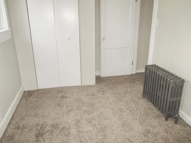 unfurnished bedroom featuring a closet, light colored carpet, and radiator