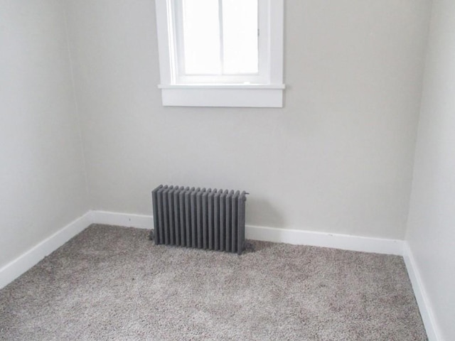 spare room featuring radiator heating unit, baseboards, and light colored carpet