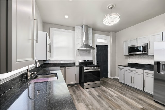 kitchen featuring white cabinets, sink, decorative light fixtures, wall chimney range hood, and stainless steel appliances