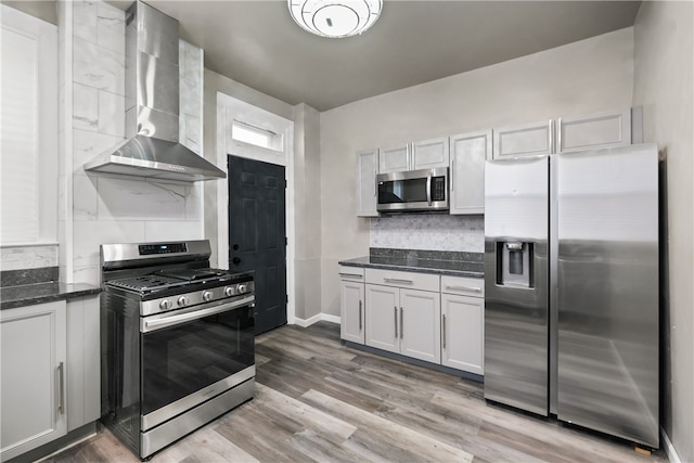 kitchen with white cabinetry, wall chimney exhaust hood, light hardwood / wood-style flooring, backsplash, and appliances with stainless steel finishes