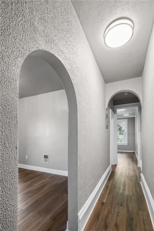 corridor with vaulted ceiling, a textured ceiling, and dark wood-type flooring