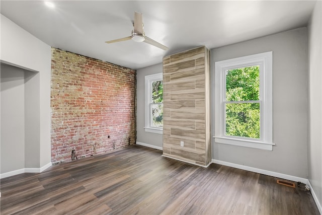 empty room featuring ceiling fan, brick wall, and dark wood-type flooring