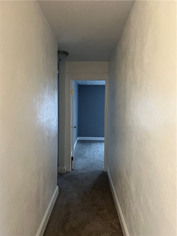 hallway with a textured ceiling and dark carpet